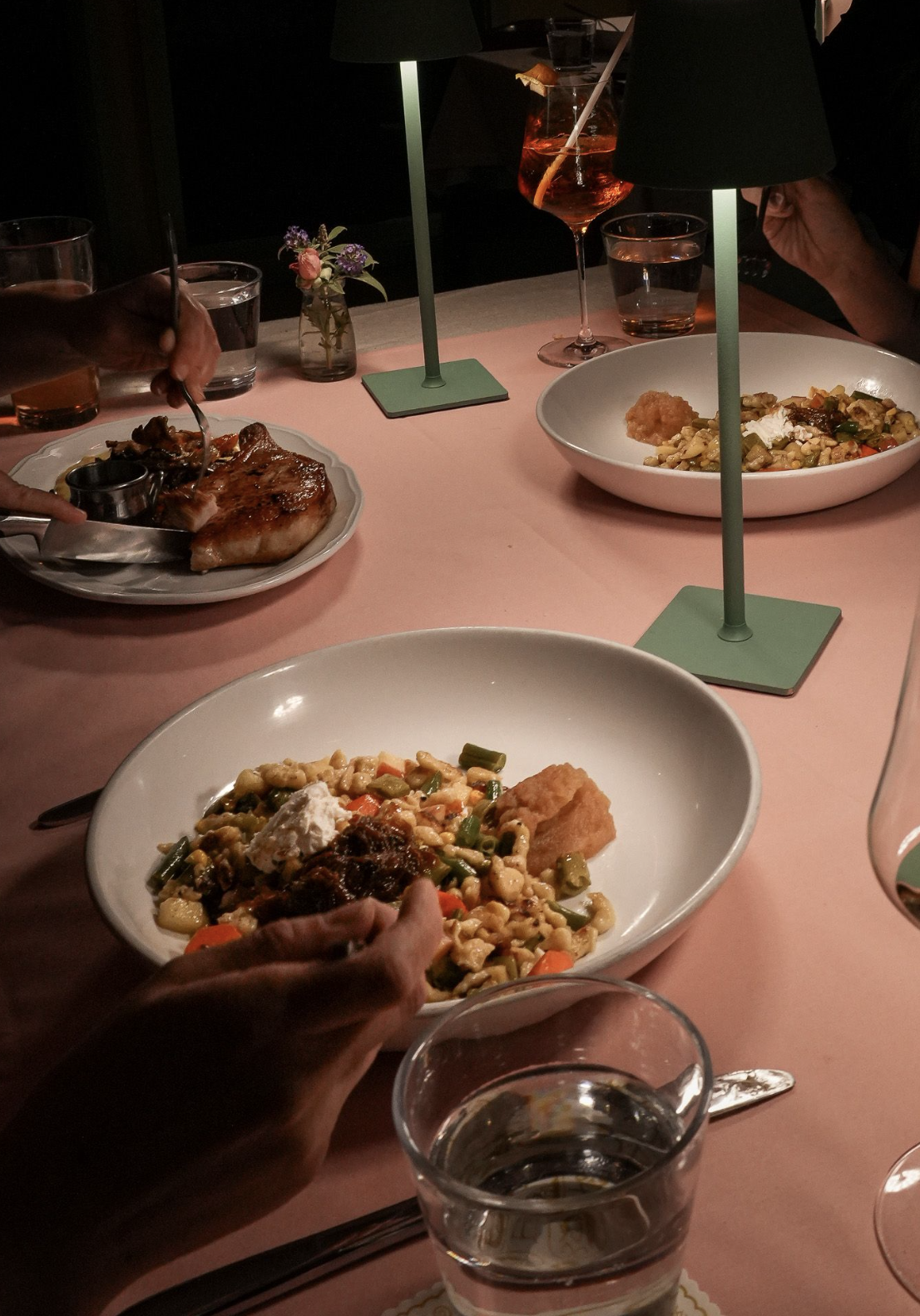 A candlelit restaurant table with shared dishes and cocktails