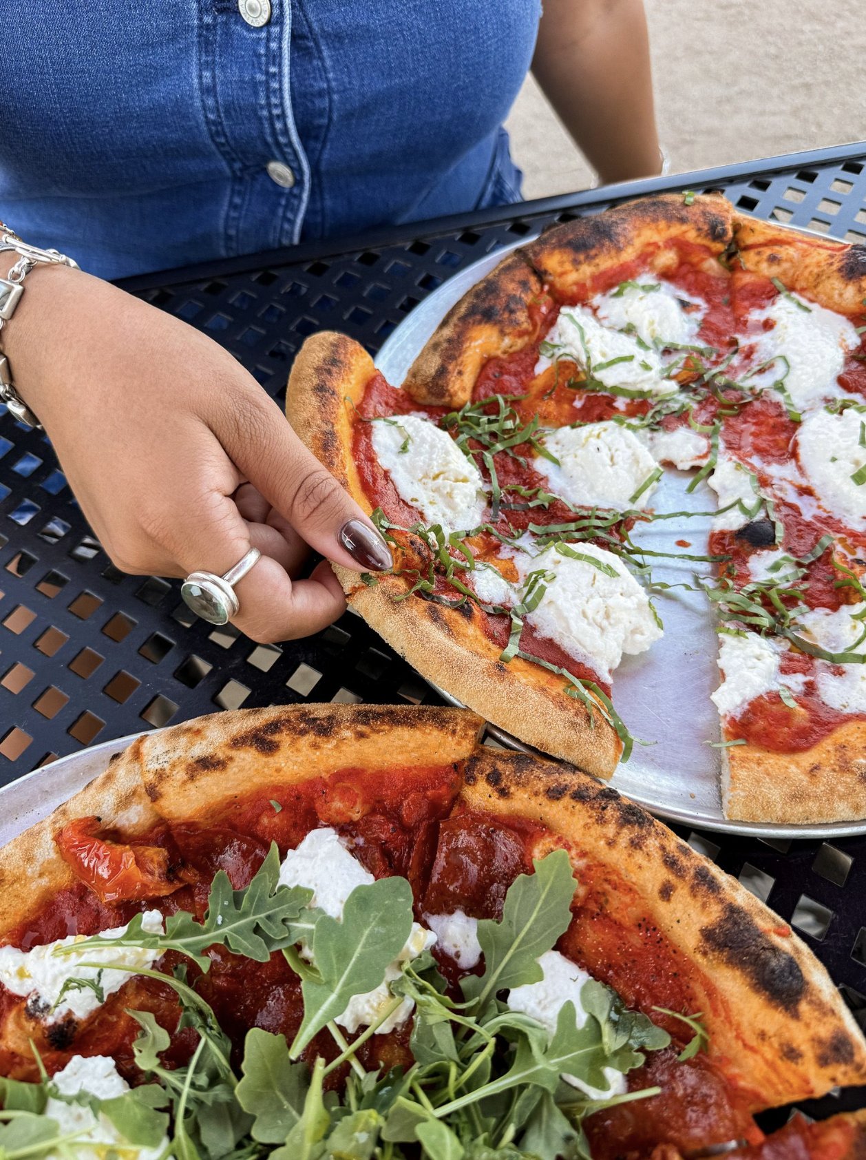 Hands sharing pizza at an outdoor restaurant table